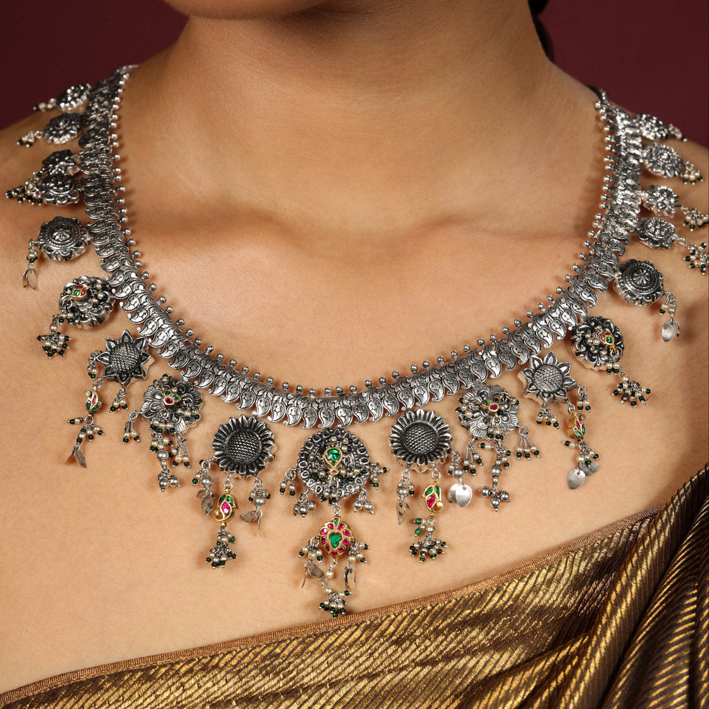 Close-up of a person wearing an ornate necklace with a blurred background